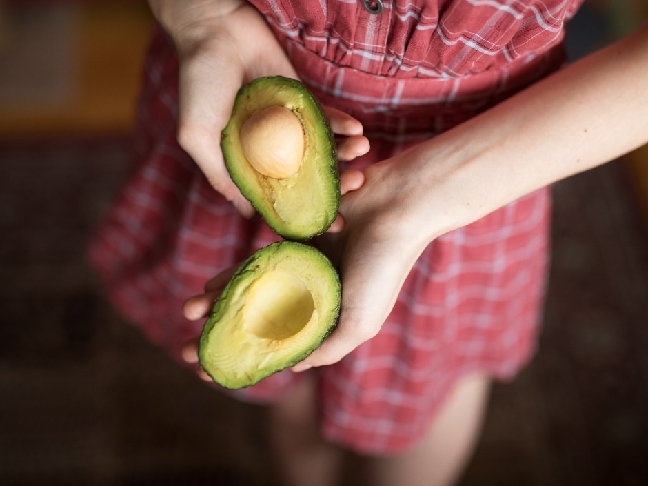 A pair of hands holding a cut avocado open.